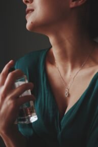 A vertical shot of a female wearing a necklace with a diamond pendant spraying perfume on her